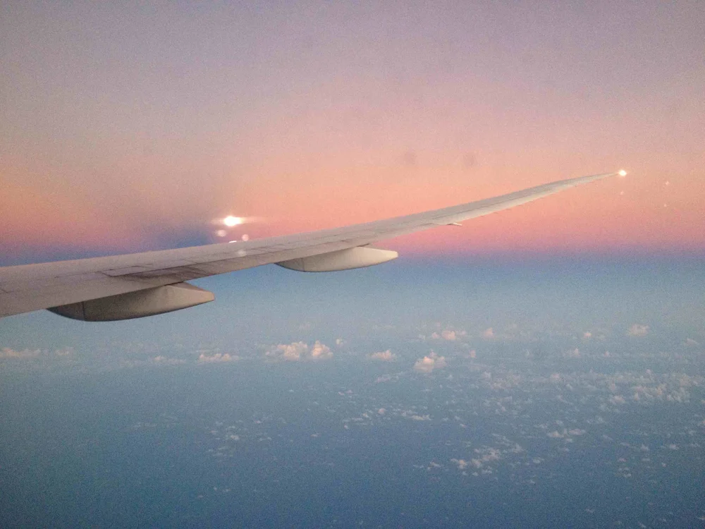 Aerial view of an airplane wing against a pastel pink and blue sunset sky with soft clouds, calm and professional mood